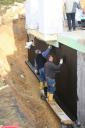 Mit der schwarzen Pampe wird auf der gemeinsamen Holzbohle die Kellerwand isoliert